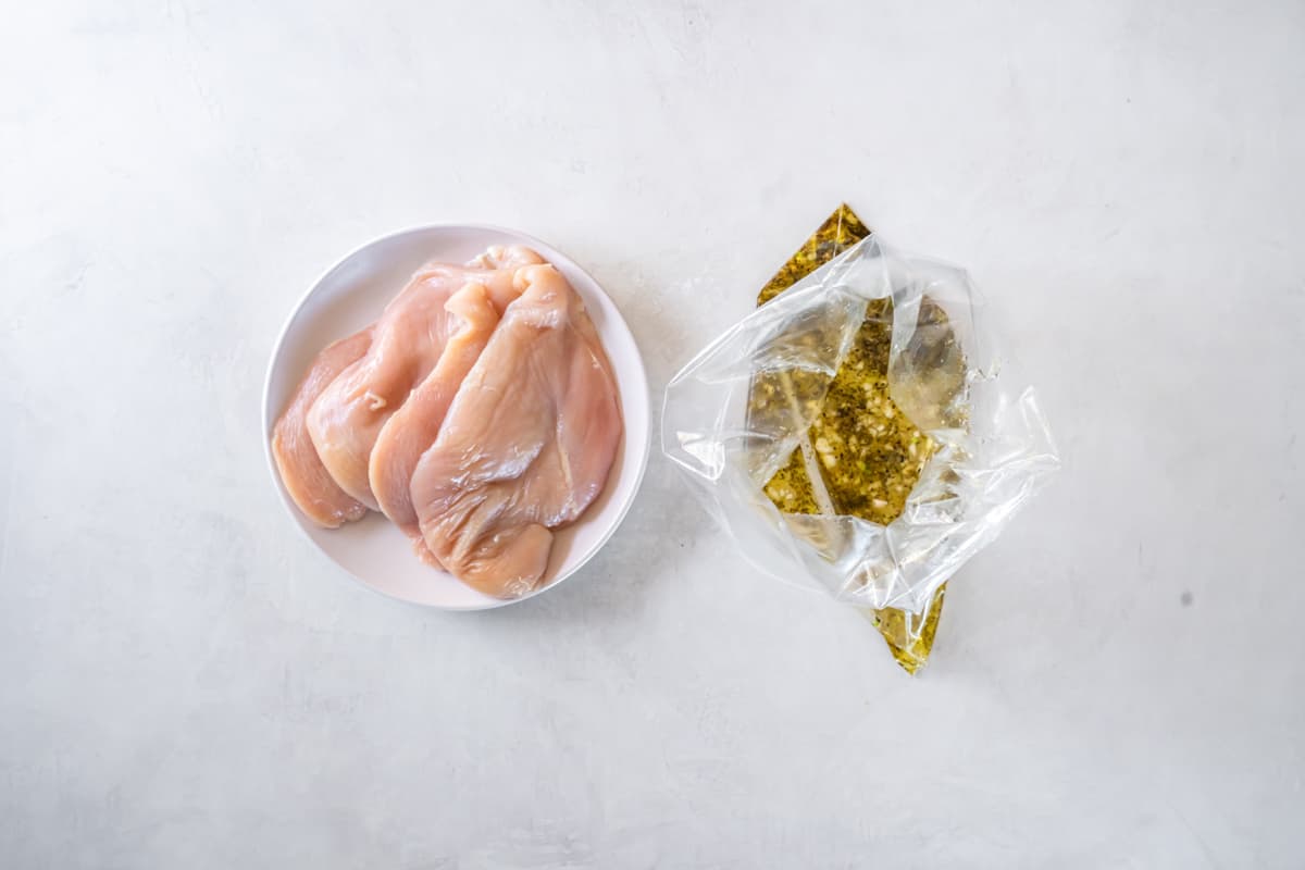 plate of raw chicken breasts next to a bag of marinade.