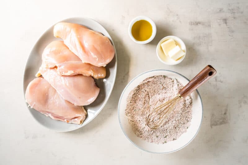 a plate of raw chicken breasts next to a bowl of seasoned flour