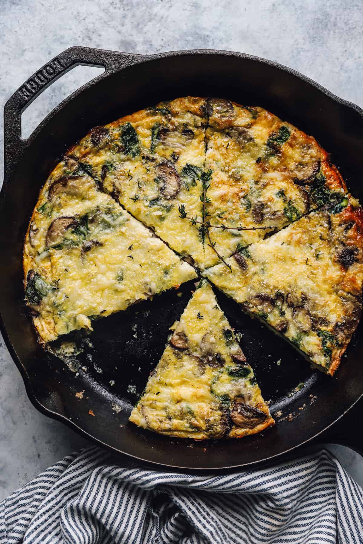 overhead view of a mushroom spinach frittata, cut into six slice, one of them has been removed from the skillet