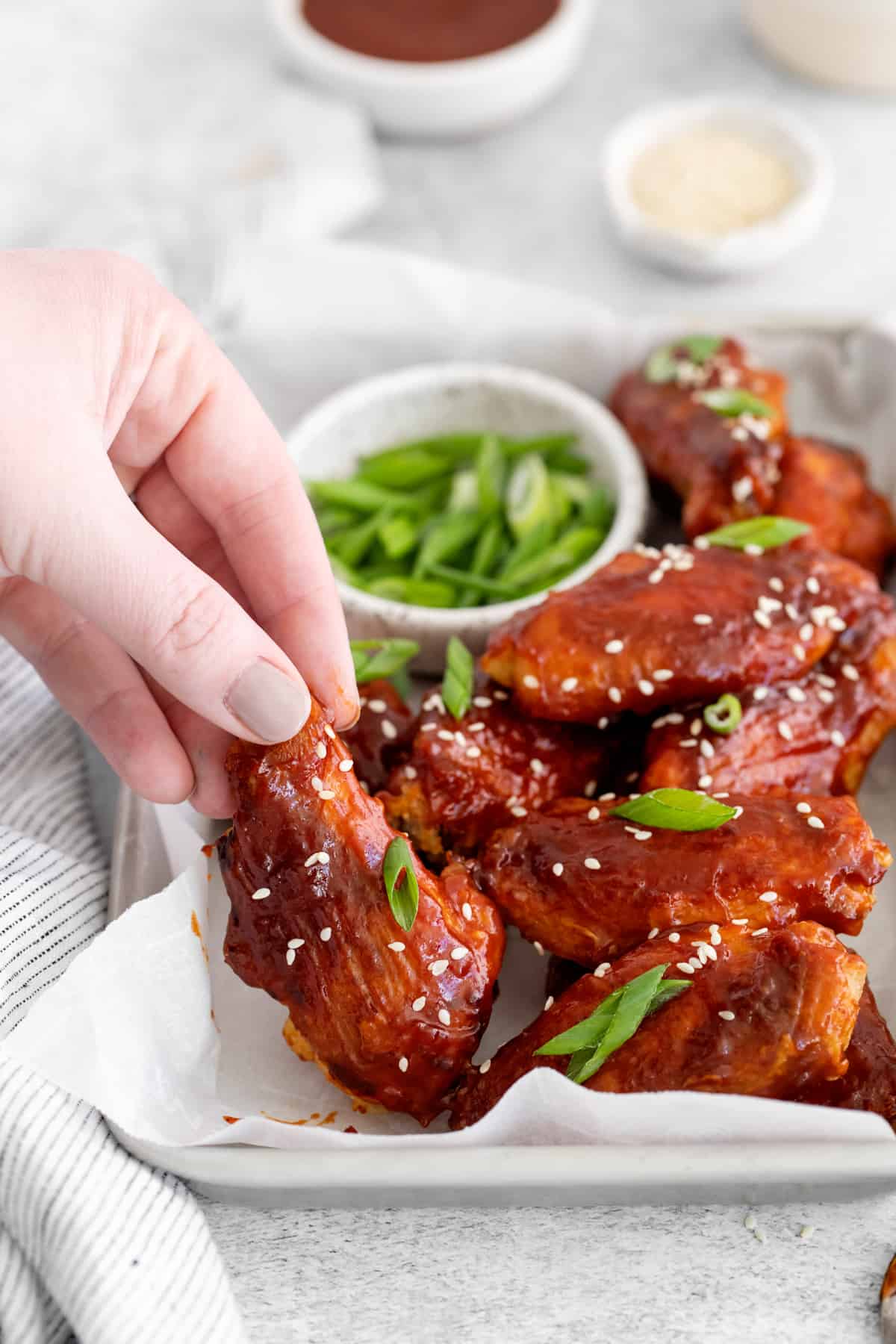 Hand picking up a Korean chicken wing from a platter.