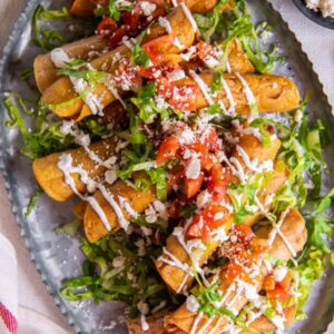 overhead view of a platter of chicken taquitos, garnished with tomatoes, lettuce, and more