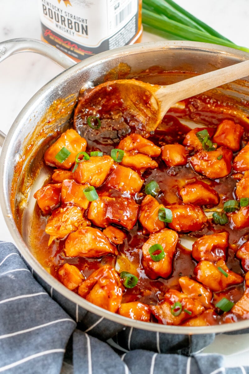 bourbon chicken in a frying pan with green onion and a wooden spoon.