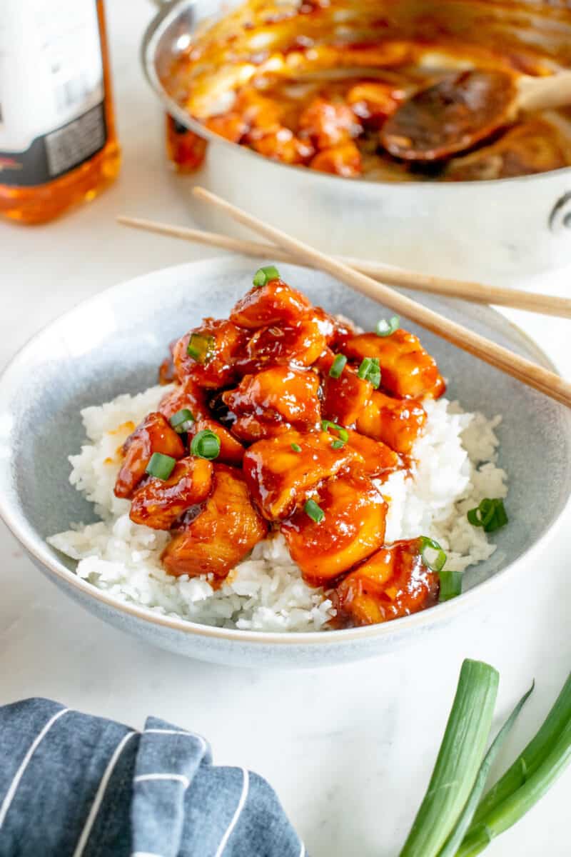bourbon chicken in a bowl with white rice and chopsticks.