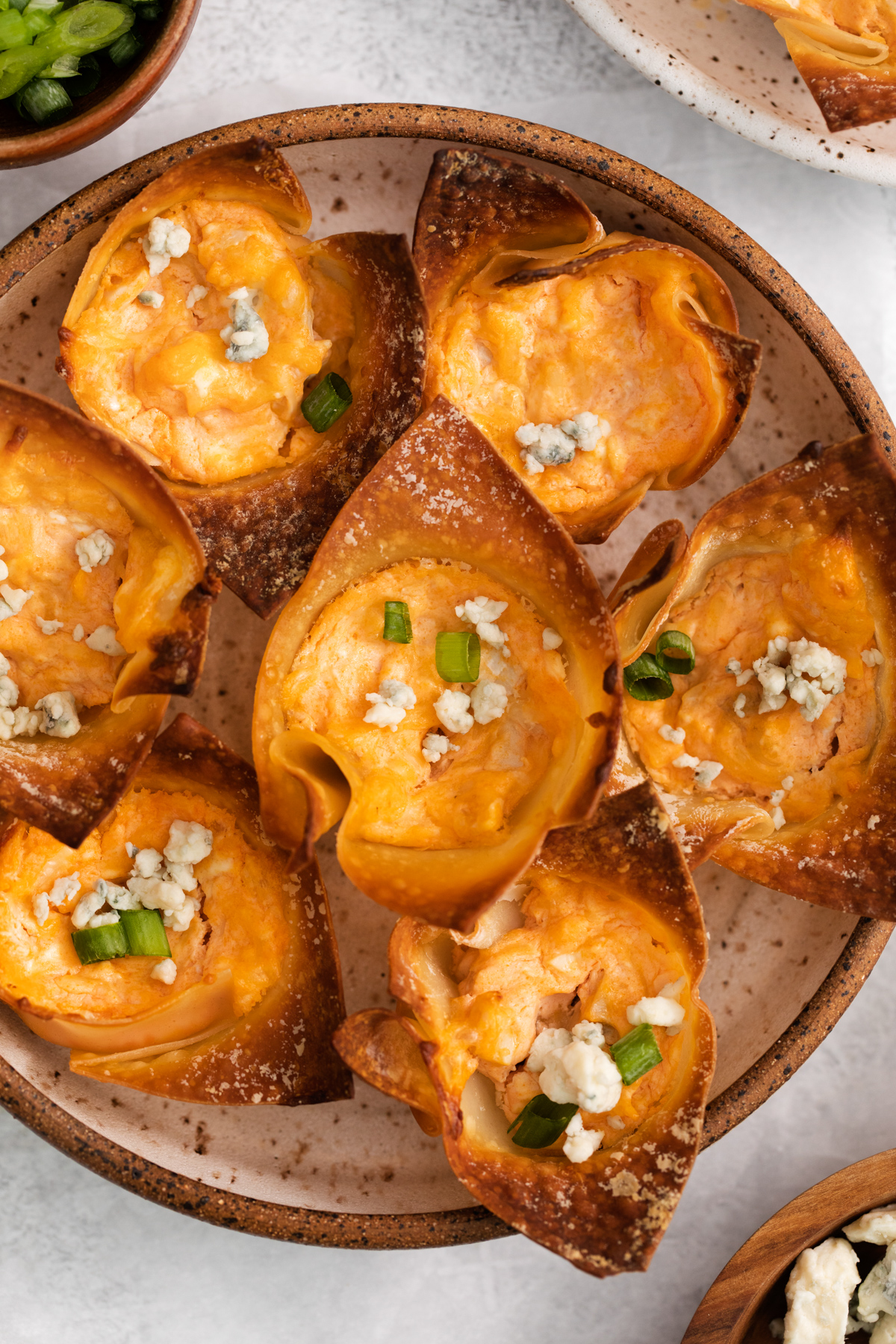 overhead view of buffalo chicken wonton cups on a white and brown plate.