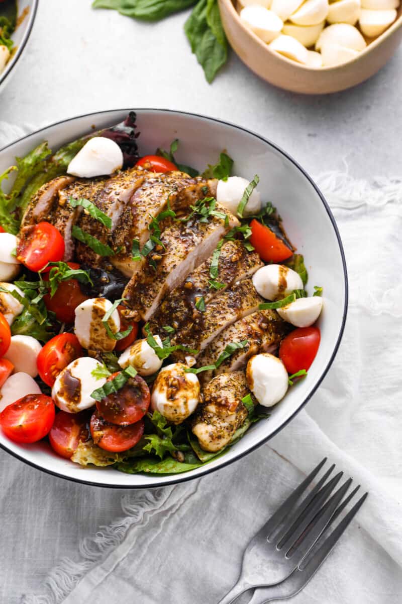 bowl of green salad with mozzarella, tomatoes, chicken, and balsamic
