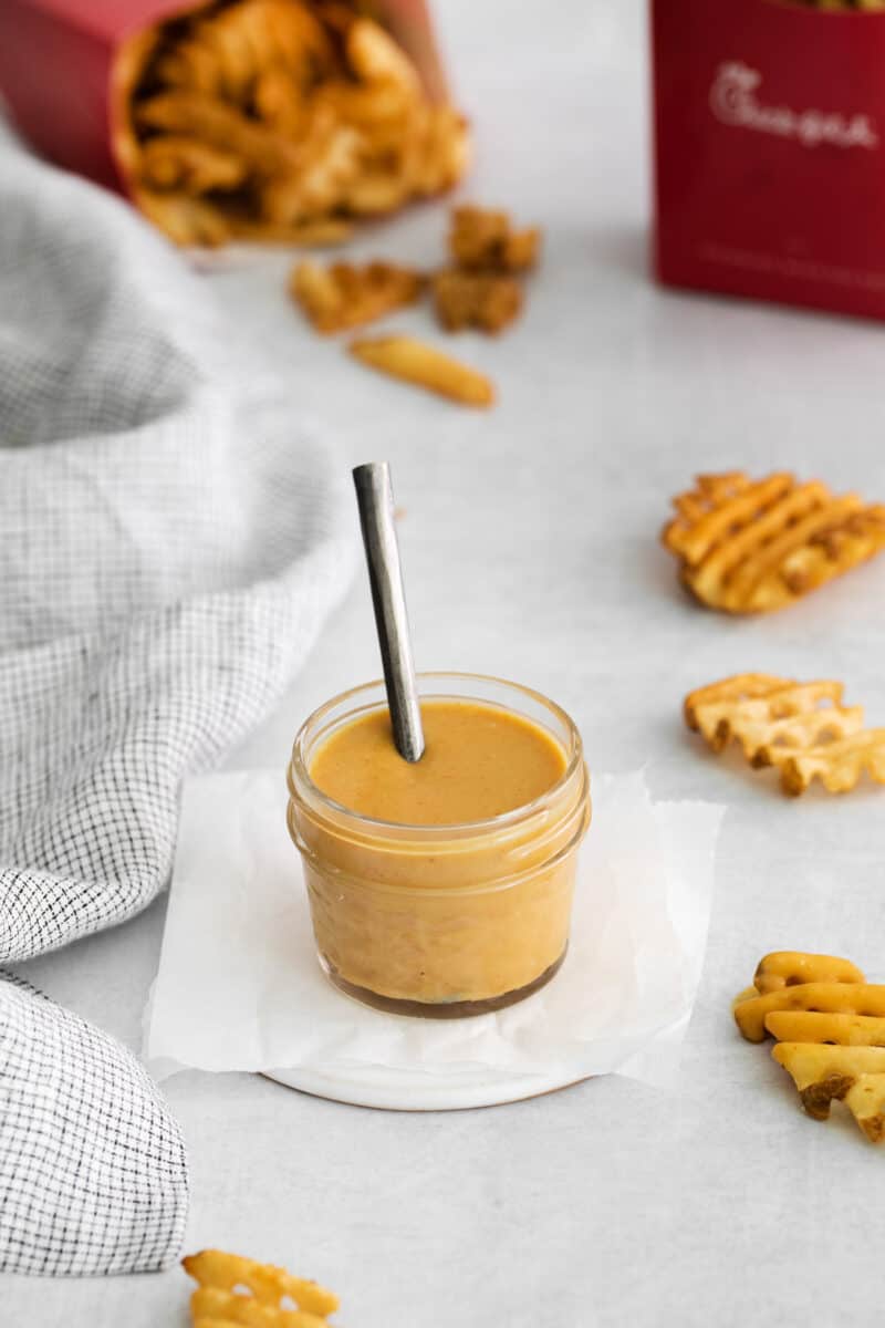 three-quarters view of chick fil a sauce in a small glass jar with a spoon on a white napkin.
