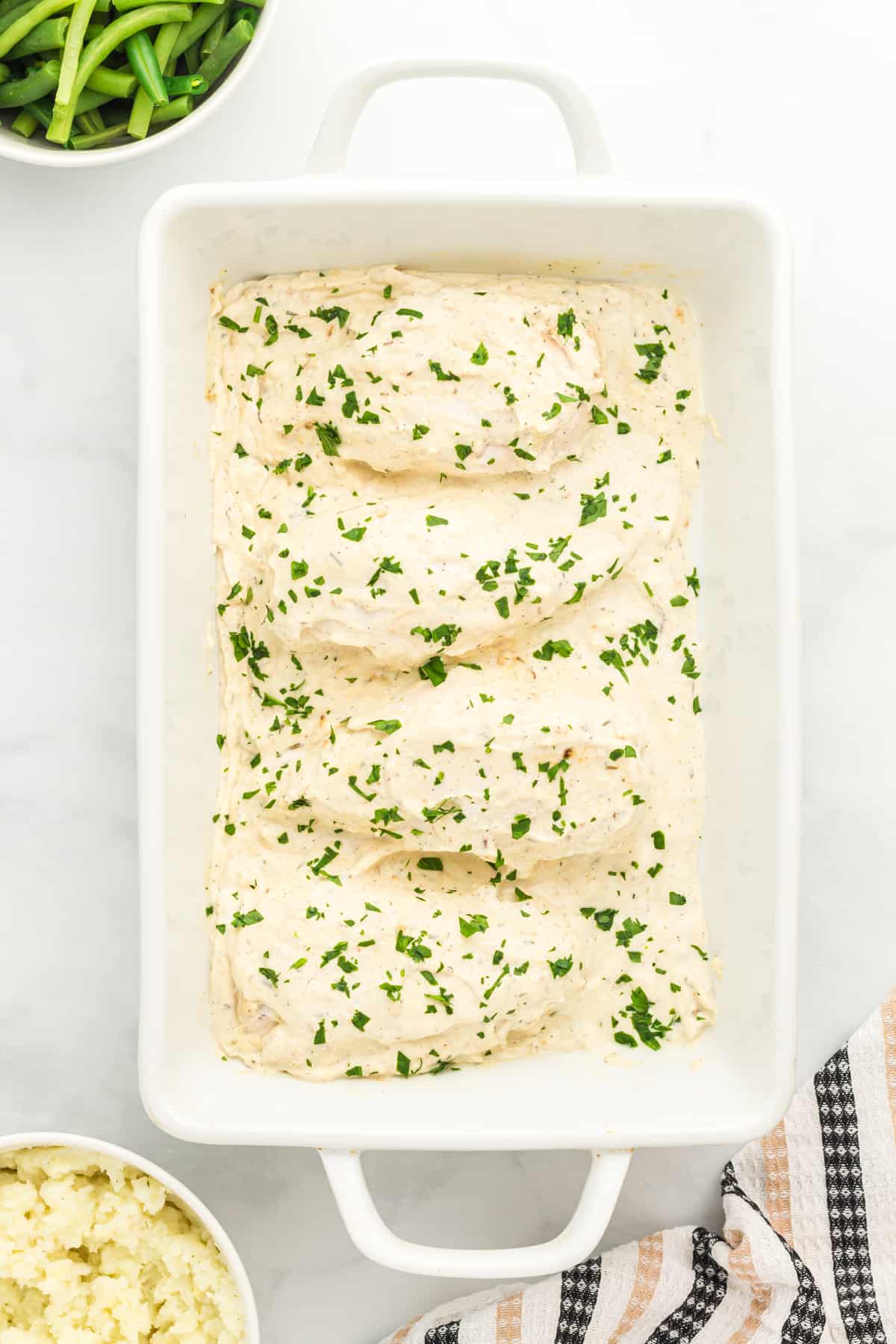 overhead view of creamy herb chicken in a white baking pan.