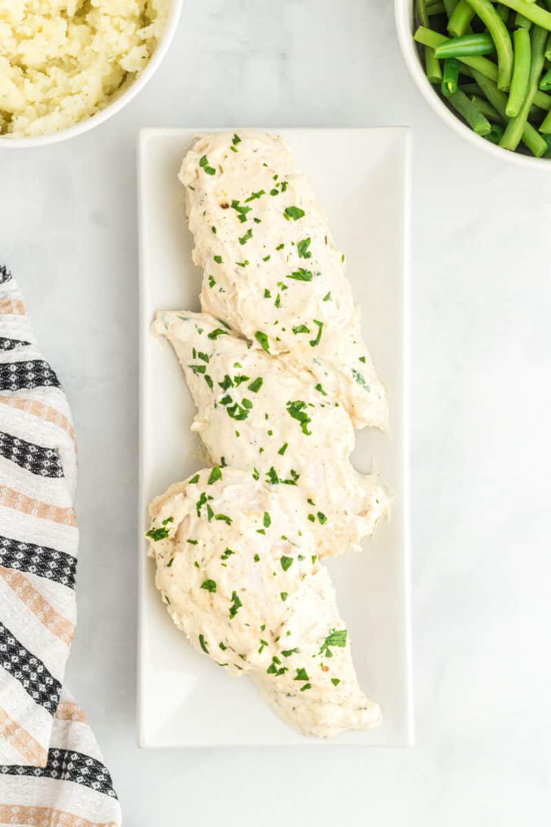 overhead view of creamy herb chicken on a white serving plate.