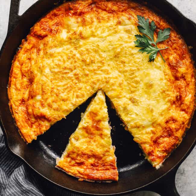 overhead view of a cut ham and cheese frittata in a cast iron pan with a small slice placed in a large gap.