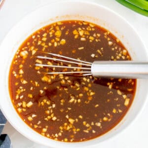 sauce for bourbon chicken in a white bowl with a whisk.