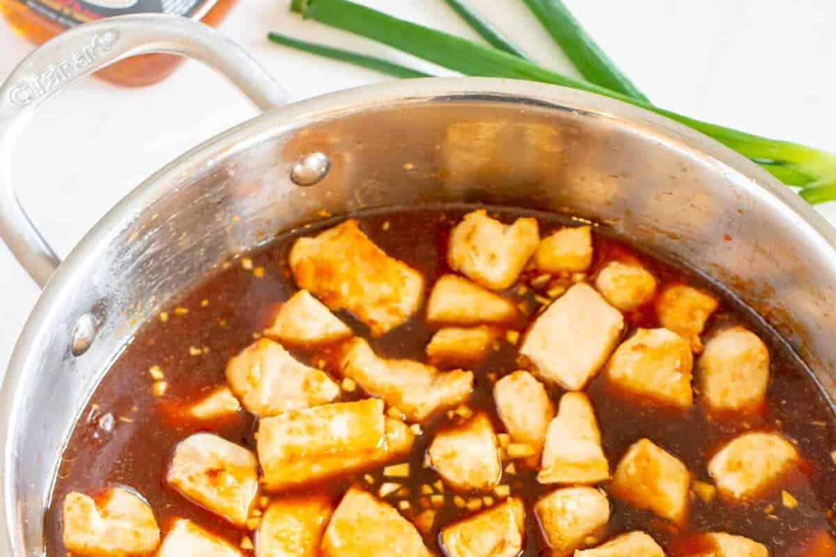 bourbon sauce poured over diced chicken in a frying pan.