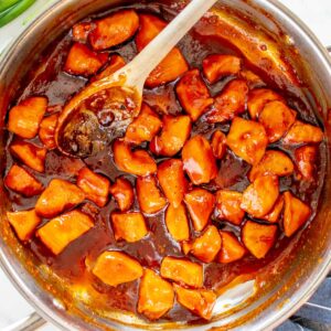 bourbon chicken in a frying pan with a wooden spoon.