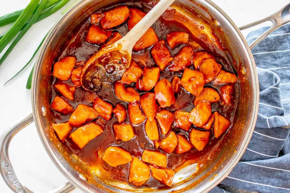 bourbon chicken in a frying pan with a wooden spoon.