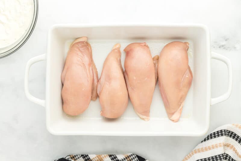 4 raw chicken breasts in a white baking pan.