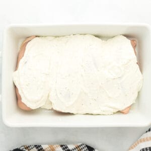 creamy herb chicken sauce poured over raw chicken breasts in a white baking pan.