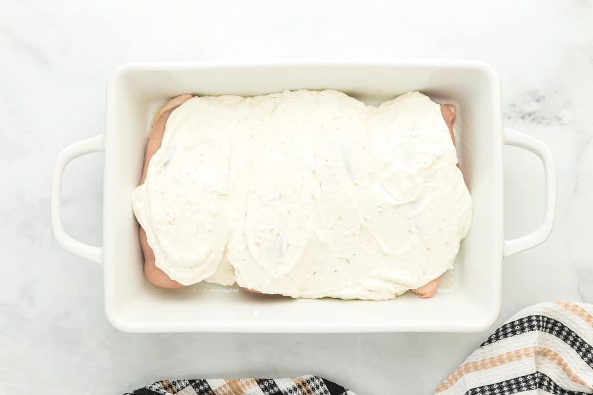 creamy herb chicken sauce poured over raw chicken breasts in a white baking pan.