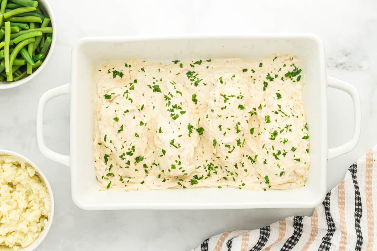 creamy herb chicken in a white baking pan.