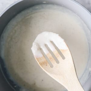 A wooden spoon is being used to stir a white sauce for a breakfast soufflé in a pan.