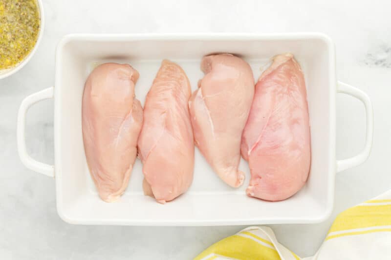 4 raw chicken breasts in a rectangular baking dish.