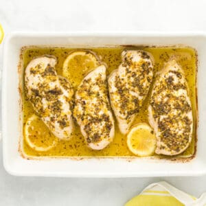 4 baked lemon butter chicken breasts in a rectangular baking dish.