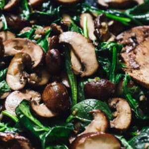 sautéed spinach and mushrooms in a pan with a wooden spoon.