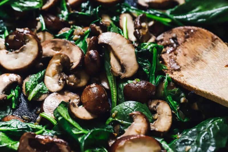 sautéed spinach and mushrooms in a pan with a wooden spoon.