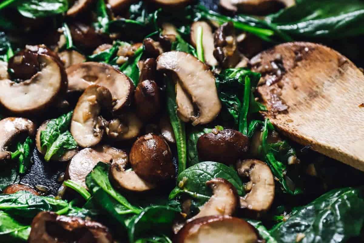 sautéed spinach and mushrooms in a pan with a wooden spoon.