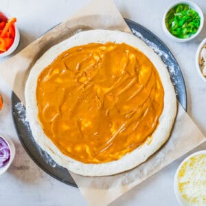 pizza dough slathered with peanut sauce, surrounded by small bowls of ingredients