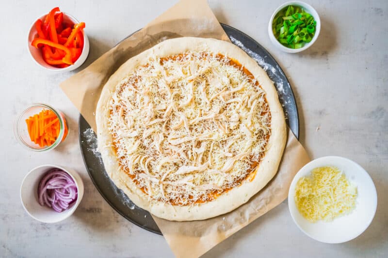 pizza crust topped with sauce, cheese, and chicken, uncooked