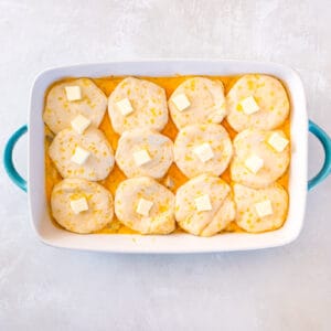 overhead view of biscuits and butter placed on top of chicken and biscuits casserole in a casserole dish.