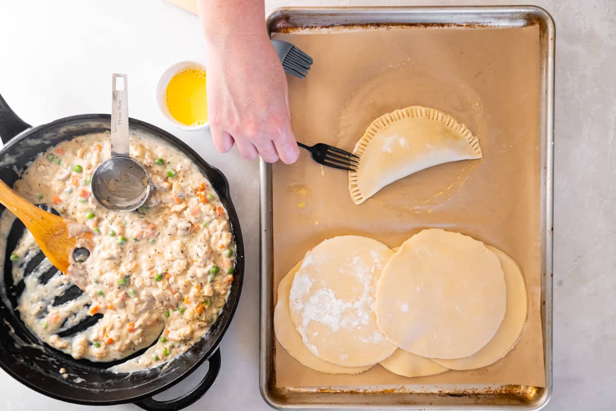 A hand using a fork to crimp the edges of a folded chicken hand pie.