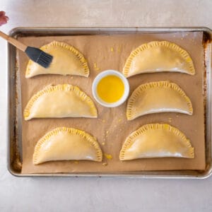 6 chicken hand pies brushed with egg wash on a baking sheet.