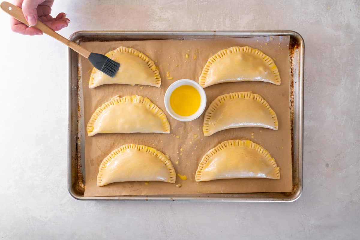 6 chicken hand pies brushed with egg wash on a baking sheet.