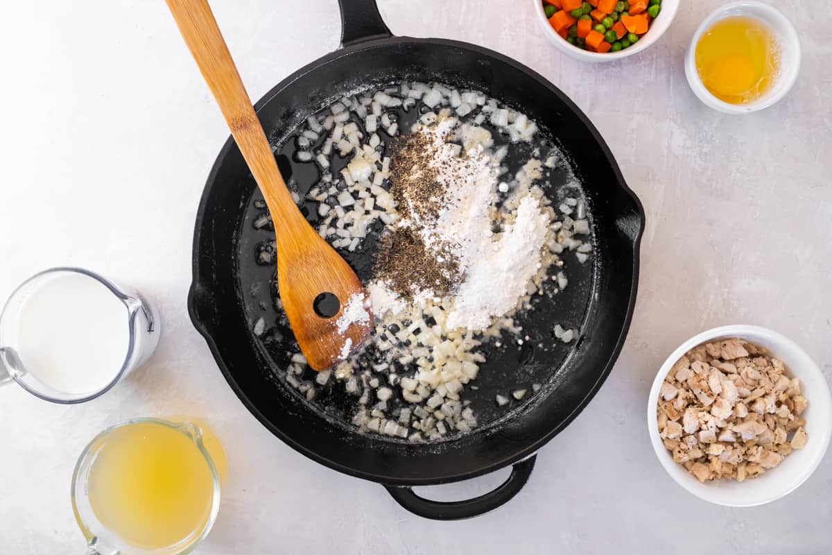 Onion and seasonings cooking in a cast iron pan with a wooden spoon.