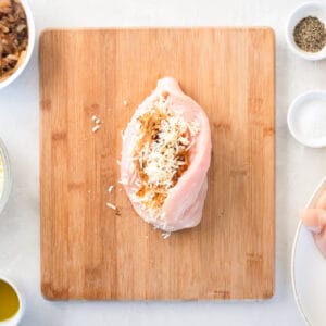 cheese and onions stuffed in a split chicken breast on a wooden cutting board.