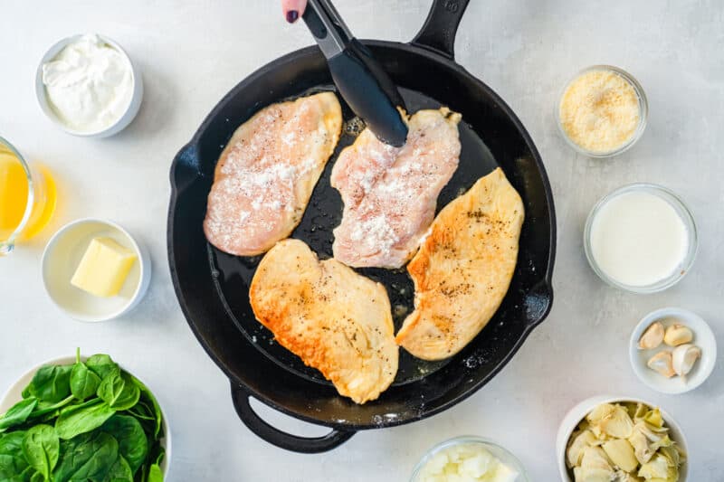 4 thin chicken breasts cooking in a cast iron skillet.
