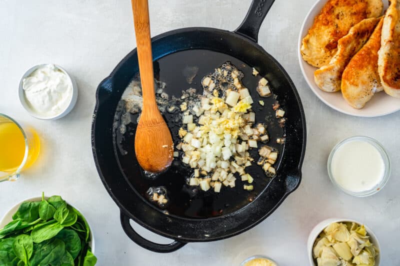 onions and garlic in a cast iron skillet with a wooden spoon.
