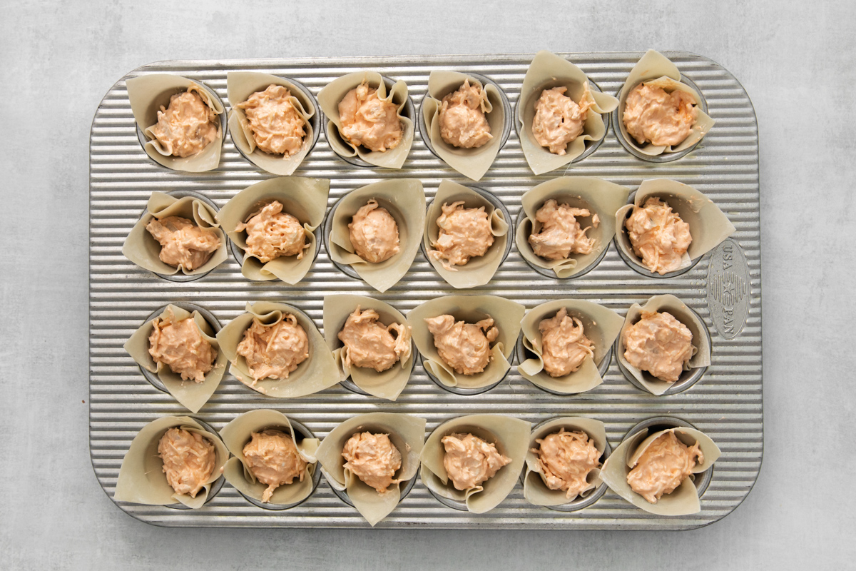Wonton cups filled with chicken mixture, in a mini muffin tin.