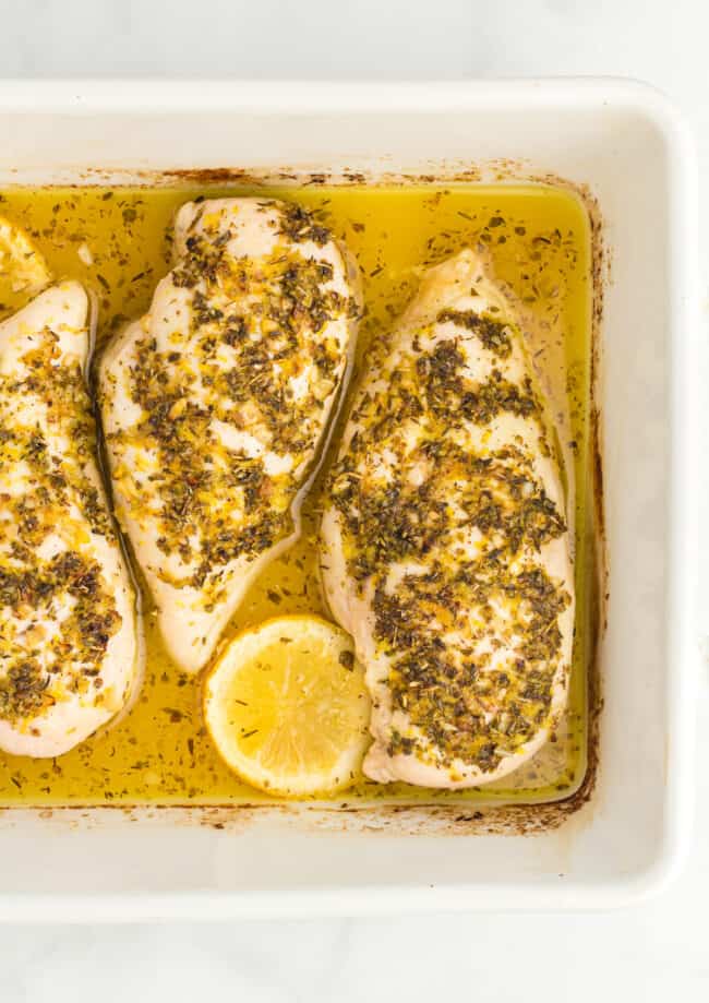 partial overhead view of baked lemon butter chicken breasts in a rectangular white baking pan.
