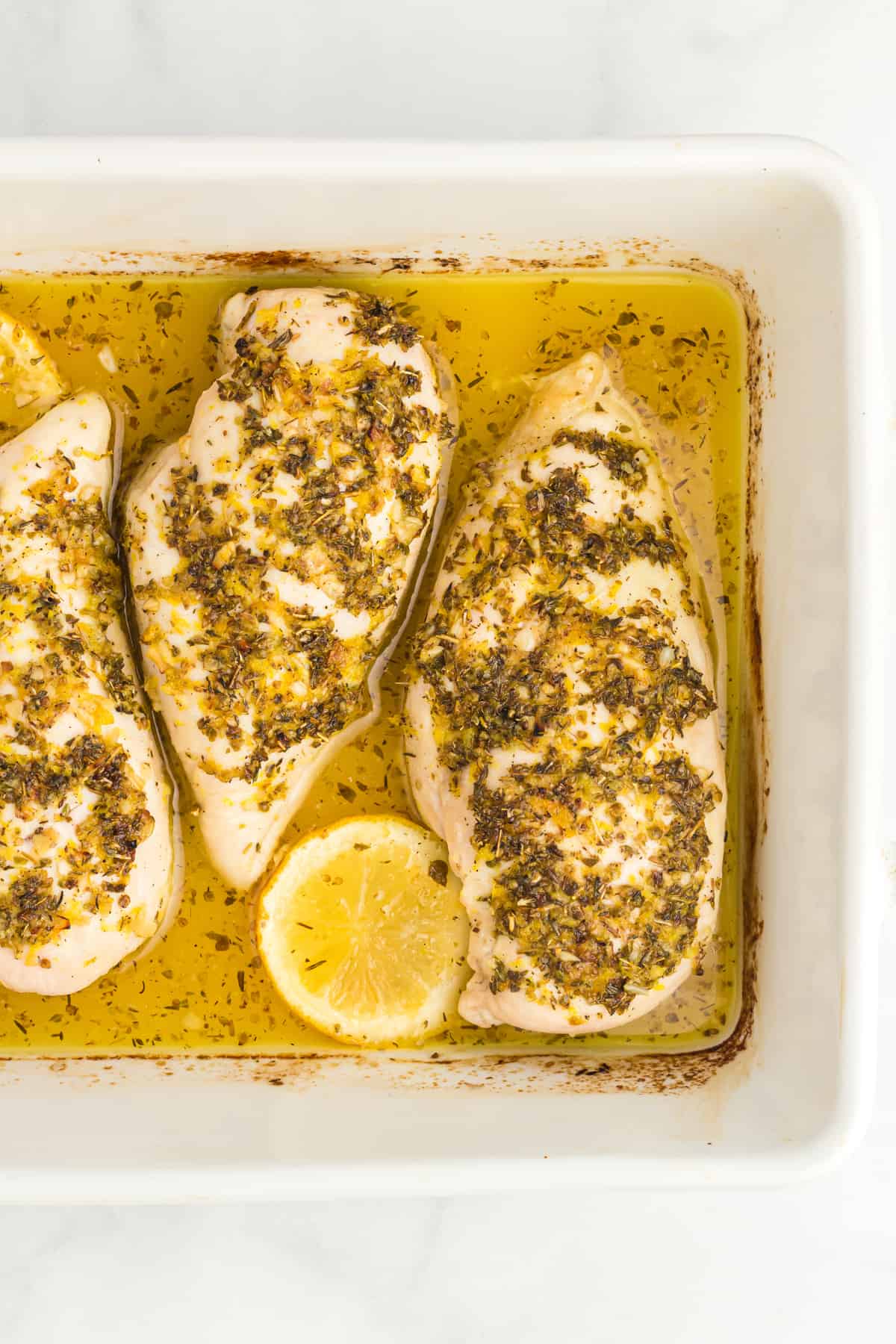 partial overhead view of baked lemon butter chicken breasts in a rectangular white baking pan.