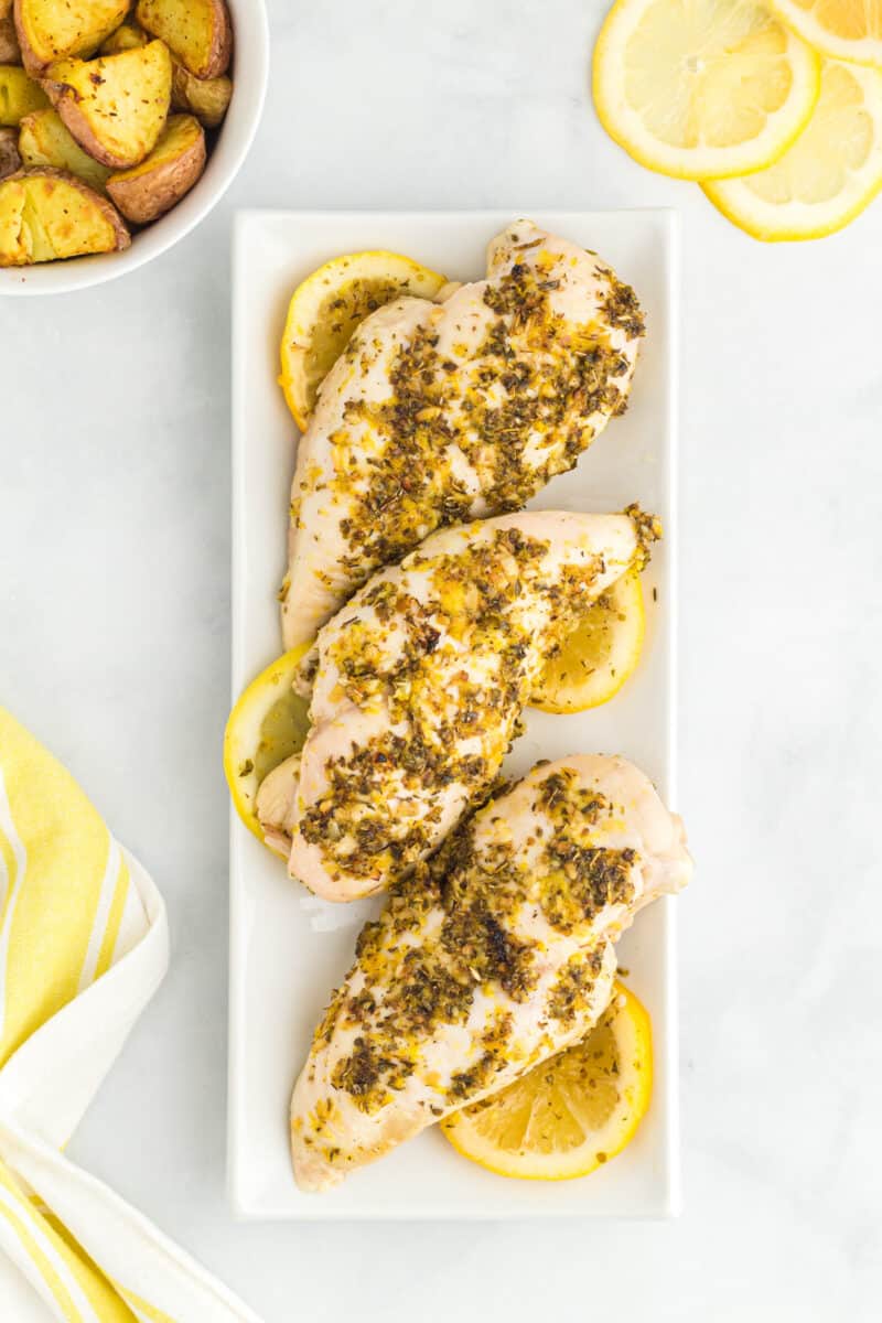 overhead view of baked lemon butter chicken breasts on a white rectangular serving tray.