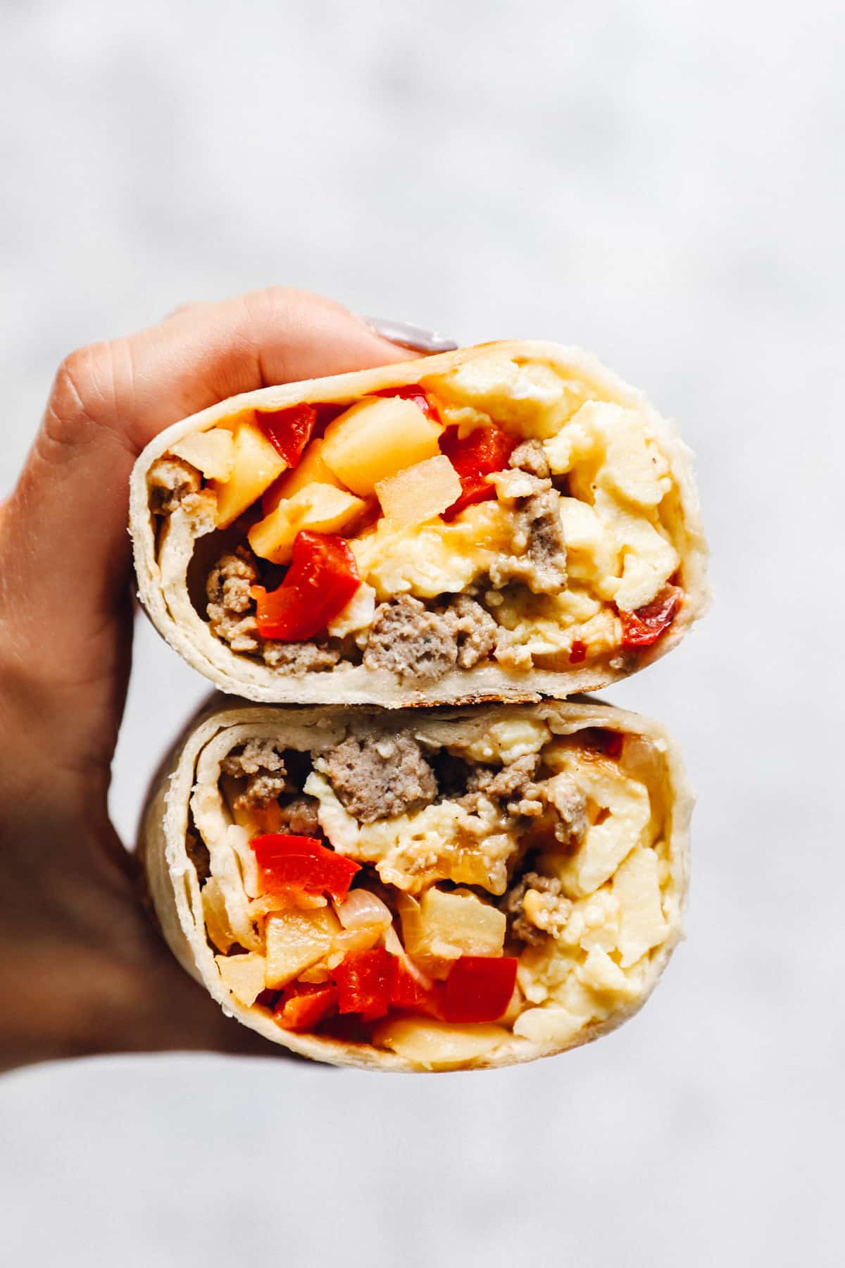 hand holding a breakfast burrito cut in half to reveal the filling