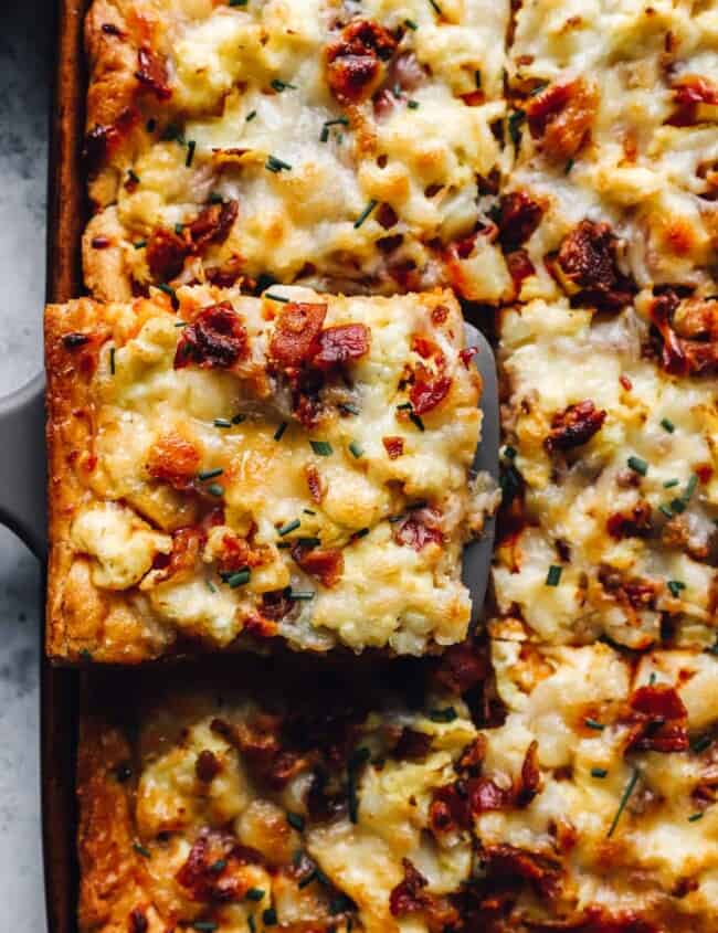 a slice of crescent roll breakfast pizza being lifted from a sheet pan by a spatula.