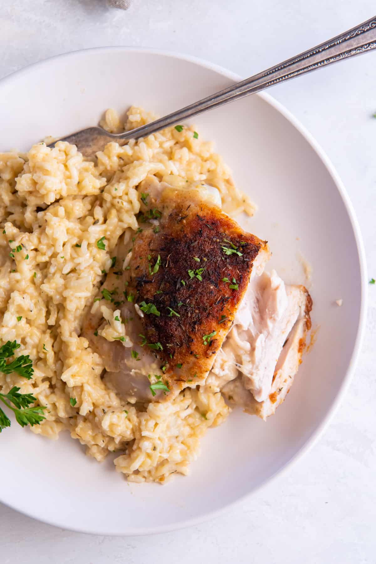 overhead view of a sliced chicken thigh on a bed of rice on a white plate with a fork.