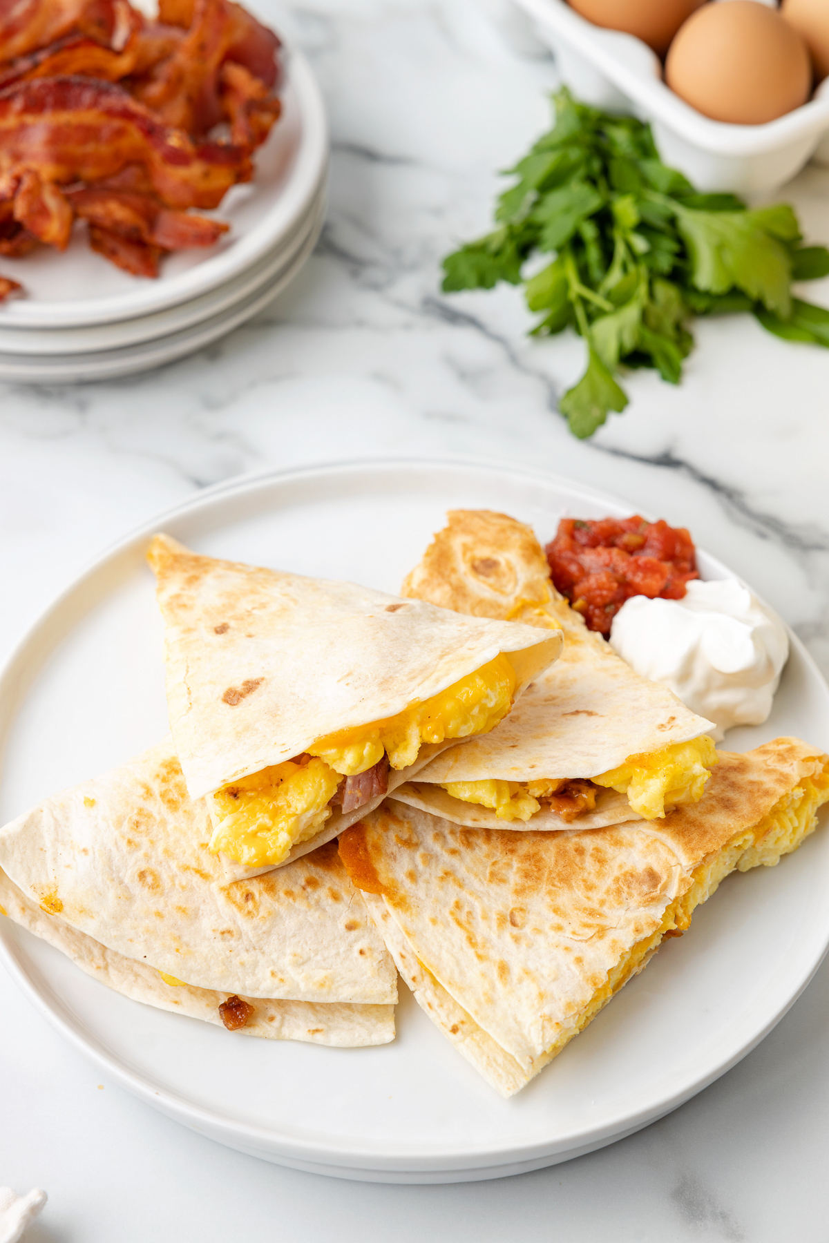 A breakfast quesadilla cut into four slices, on a plate with sour cream and salsa.
