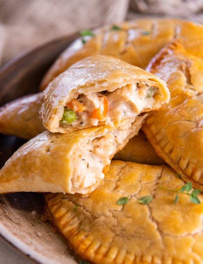 a halved chicken hand pie stacked on itself to show the filling on a pile of chicken hand pies.