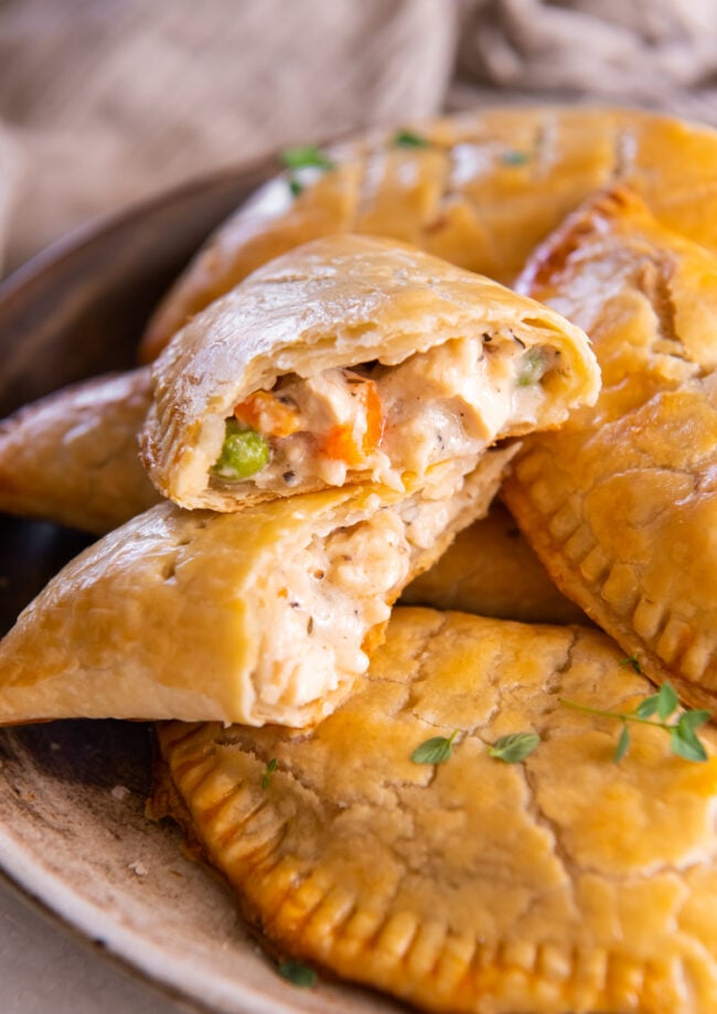 a halved chicken hand pie stacked on itself to show the filling on a pile of chicken hand pies.