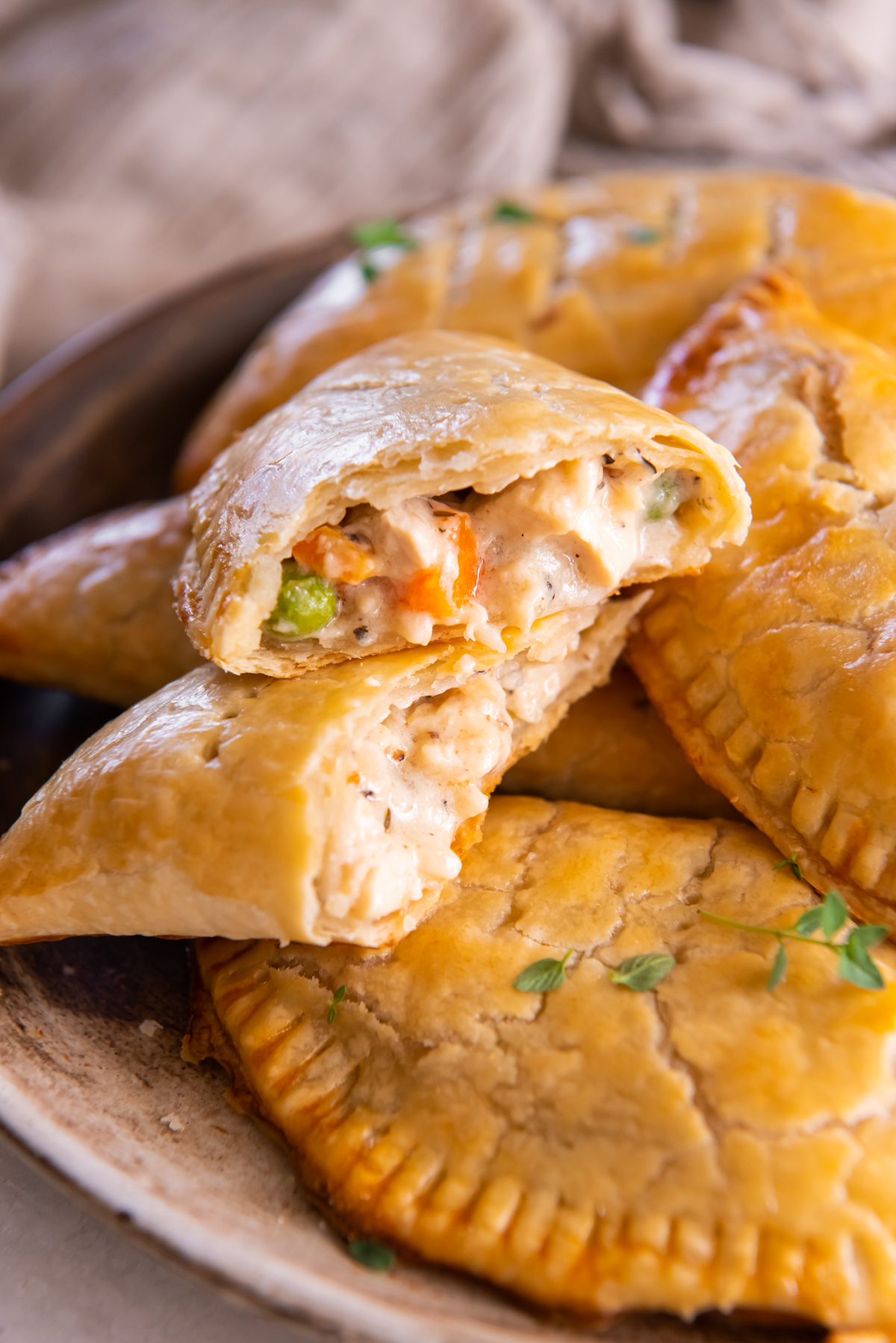 a halved chicken hand pie stacked on itself to show the filling on a pile of chicken hand pies.
