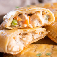 close up of a halved chicken hand pie exposed to show the filling on top of a stack of chicken hand pies.