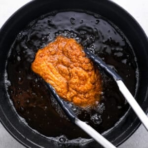 tongs grabbing fried chicken out of a pot of oil